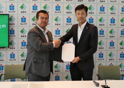 固い握手を交わす学校法人松山大学溝上理事長と西条市玉井市長
